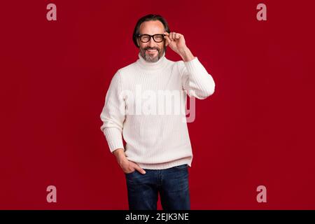 Foto-Porträt von fröhlichen alten Mann berühren Brillen in stilvollen Look lächelnd isoliert auf rotem Hintergrund. Stockfoto