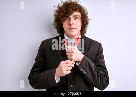Erschrockener Mann auf einer Bühne mit Mikrofon, lockiges Männchen hat Angst vor dem öffentlichen Sprechen. Isoliert auf weiß Stockfoto