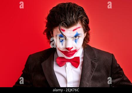 Portrait von virile harten Illusionist mit bunten Make-up selbstbewusst Blick auf die Kamera, Zauberer in Anzug isoliert auf rotem Hintergrund Stockfoto