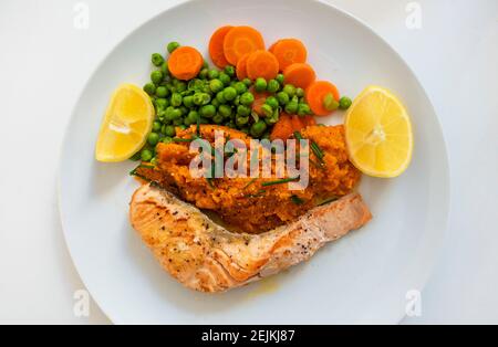 Gegrilltes Lachsfilet mit Erbsen und Karotten, Kartoffelpüree, Schnittlauch und Zitrone Stockfoto