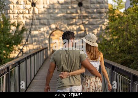 Rückansicht eines jungen Paares, das am späten Nachmittag im September bei Sonnenuntergang auf einer hölzernen Plattform der Hängebrücke des Aare-Flusses umarmt ging. Stockfoto