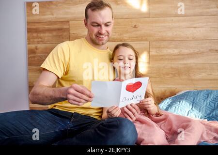 Junger Papa am Vatertag erhielt von fürsorglichen Tochter Papier Postkarte schriftliche Nachricht besten Wünsche, gezeichnet roten Herzen als Symbol der Liebe und tiefe affecti Stockfoto
