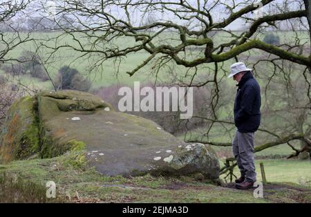 Mann, der die Inschrift auf einem Felsen bei Stanton Moor liest Im Peak District Stockfoto