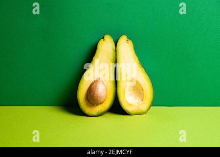 Ganze reife Avocado in der Nähe halbierte Früchte vor grünem Hintergrund Stockfoto