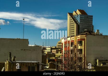 Blick auf die Dächer von dicht bebauten Teheran mit einem Blick auf ein Hochhaus mit blauer Glasfassade Gegen einen blauen Himmel Stockfoto