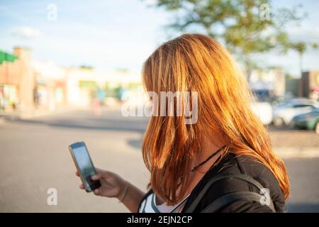 Mutter, die an einem sonnigen Tag ihr Telefon überprüft Ein Parkplatz, auf dem ihr Kontostand überprüft werden kann Unterwegs mit Fernzugriff auf ihr persönliches Online-Gerät Stockfoto
