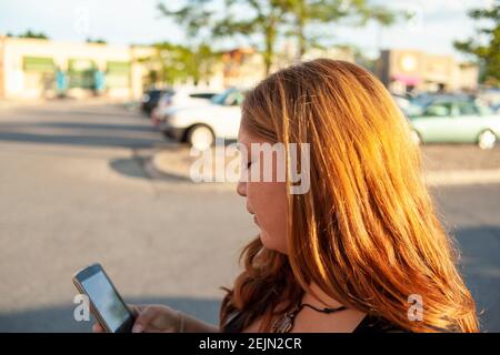 Mutter, die an einem sonnigen Tag ihr Telefon überprüft Ein Parkplatz, auf dem ihr Kontostand überprüft werden kann Unterwegs mit Fernzugriff auf ihr persönliches Online-Gerät Stockfoto
