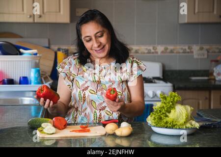 Hispanische Frau, die Gemüse zum Kochen wählt - lächelnd mittleren Alters Frau, die frischen Bio-Salat in ihrer Küche Stockfoto