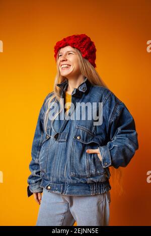 Lächelnde junge Frau in warmen Kleidern vor hellorangefarbenem Hintergrund Stockfoto