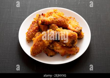 Hausgemachte würzige Mango Chicken Wings auf einem weißen Teller auf schwarzem Hintergrund, Seitenansicht. Stockfoto