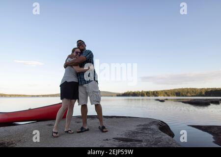 Paar umarmen und umarmen auf felsigen See Ufer in Maine Mit Kanu Stockfoto