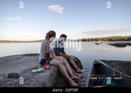Interracial paar sitzen am Seeufer mit Kanu und kochen Abendessen Stockfoto