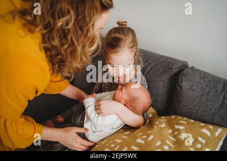 Mutter hilft älteren Tochter neugeborenes Baby auf dem Sofa zu halten Zu Hause Stockfoto