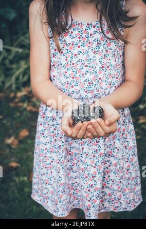 Kind in einem Blumenkleid hält Schokolade gesunde Leckereien oder Glückselsbällchen in einem Garten Einstellung. Stockfoto