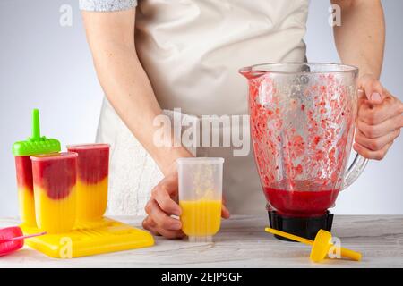 Eine Mutter bereitet hausgemachte alle natürlichen Fruchtpopsicles. Sie füllt bpa-freie Plastikformen mit Schichten pürierten Mango und Beerenmedley vor Stockfoto