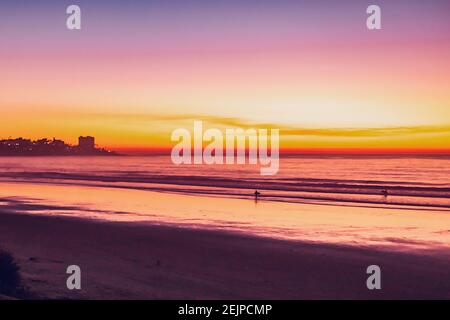 Der Strand in der Abenddämmerung mit Schattierungen von Gelb und Orange am Horizont. Stockfoto