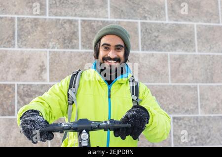 Junger Mann mit Bart draußen mit Winterjacke und Roller in Schnee Stockfoto