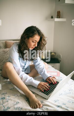 Junge Frau arbeitet an ihrem Laptop im Bett. Stockfoto