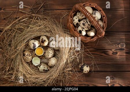 Mehrere Wachteleier im dekorativen Nest des Strohs und im Korb auf dem hölzernen Tisch, flachlegen. Stockfoto