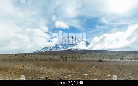 Panoramaaufnahme des schneebedeckten Chimborazo-Vulkans mit blauem Himmel und Wolken. Konzeptreise in Ecuador, Südamerika Stockfoto