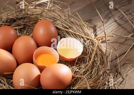 Mehrere rohe frische Hühnereier in einem Heu-Nest auf einem hölzernen Hintergrund. Stockfoto