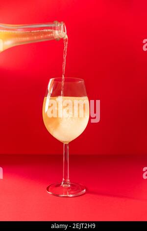 Glänzender Champagner, der in Glas auf rotem Hintergrund eingießt. Neujahr, Weihnachten, Valentinstag, Frauentag oder Muttertag festliche Karte mit Copyspace Stockfoto