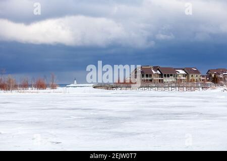 Eine alte Holzbrücke überquert einen Abschnitt der gefrorenen Georgian Bay Waterfront in Collingwood, Ontario. Der Himmel oben ist bedrohlich und düster, mit dem Winter Stockfoto