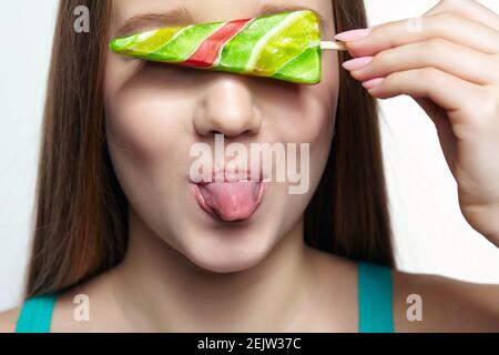 Teenager-Mädchen mit Lollipop in den Händen schließen Augen und zeigen Zunge. Naschkatzen-Konzept. Stockfoto