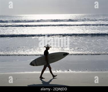 AsiaIndonesia, Bali, Kuta Beach, Silhouette von Surfer Walking entlang Strand bei Sonnenuntergang Stockfoto