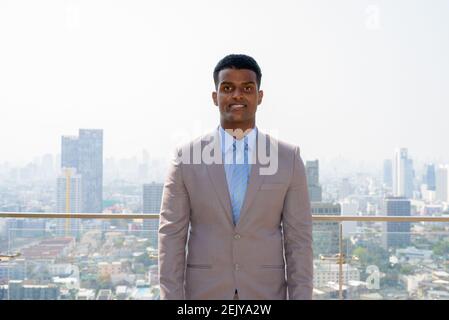 Portrait eines hübschen jungen afrikanischen Geschäftsmannes, der Anzug trägt, während er lächelt Stockfoto