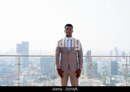 Porträt eines hübschen jungen afrikanischen Geschäftsmannes in Anzug auf dem Dach Blick auf die Stadt Stockfoto