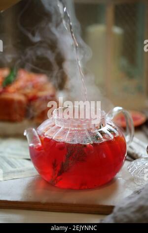 Kochendes Wasser wird in eine Glas-Teekanne mit Preiselbeeren gegossen Stockfoto