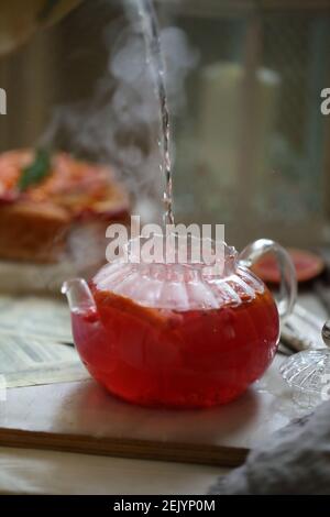 Kochendes Wasser wird in eine Glas-Teekanne mit Preiselbeeren gegossen Stockfoto