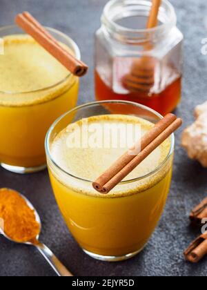 Gesunde trinken goldene Kurkuma Latte in Glas.Goldmilch mit Kurkuma, Ingwerwurzel, Zimtstangen, getrocknete Kurkuma Pulver und Honig über schwarzem Zement Hintergrund.Detox Kurkuma Tee und Zutaten. Stockfoto