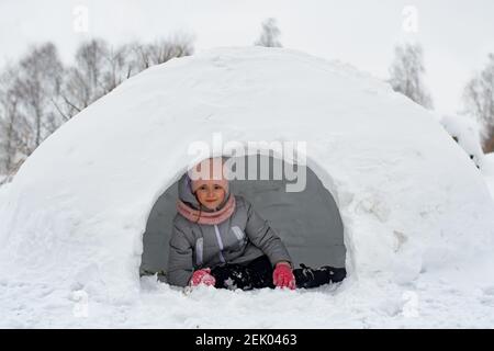 Mädchen in Winterkleidung liegen auf dem Schnee in der Nähe der Eingang zum Iglu Stockfoto