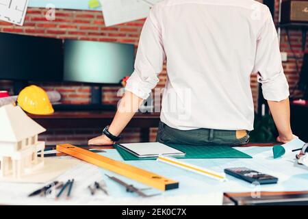 Industriemanager, Ingenieur, Geschäftsmann sitzen auf dem Tisch und überprüfen Blaupause, Zeichnung Plan an der Wand im Raum im Büro. Stockfoto