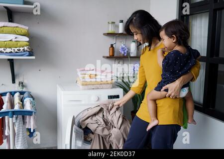 Mutter eine Hausfrau mit einem Baby beschäftigt in der Wäscherei mit Waschmaschine Stockfoto