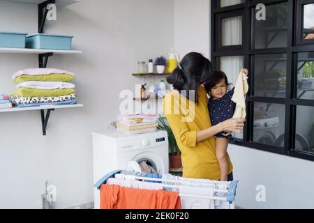 Mutter eine Hausfrau mit einem Baby beschäftigt in der Wäscherei mit Waschmaschine Stockfoto