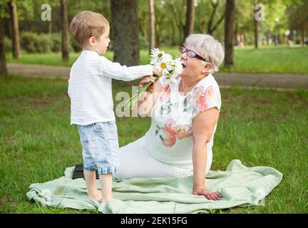 Kleiner Junge mit Blumen und seine Großmutter im Park. Alles gute zum Muttertag Stockfoto