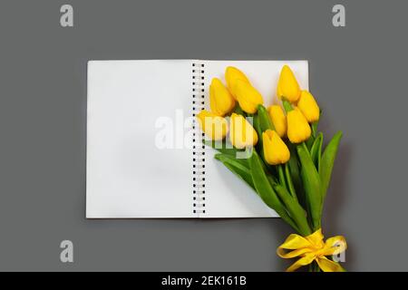 Öffnen Sie leeren Notizblock und Bouquet von gelben Tulpenblüten auf grauen Tisch Draufsicht. Flach legen. Stockfoto