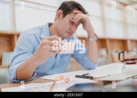 Geschäftsmann Kopfschmerzen und halten Haftnotiz mit Text "MÜDE". Müde, überfordert nach langer Zeit mit Laptop im Büro. Stockfoto