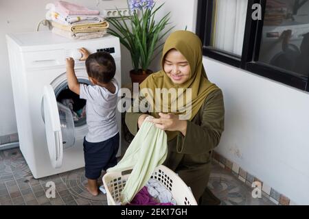 muslimische Mutter eine Hausfrau mit einem Baby in der Wäscherei beschäftigt Mit Waschmaschine Stockfoto