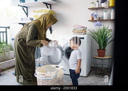 muslimische Mutter eine Hausfrau mit einem Baby in der Wäscherei beschäftigt Mit Waschmaschine Stockfoto