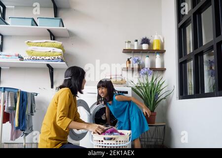 Schöne junge asiatische Frau und Kind Mädchen kleinen Helfer tun Wäsche zu Hause. Stockfoto