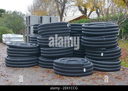 Rollen von schwarzen gewellten flexiblen Ablaufrohren auf einer Baustelle im Nordosten Italiens. Stahlbeton quadratische Kasten Culverts sind im Hintergrund Stockfoto