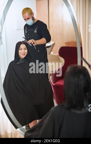 Professionelle Friseur in einer Gesichtsmaske Kämmen seine Client Haar Stockfoto