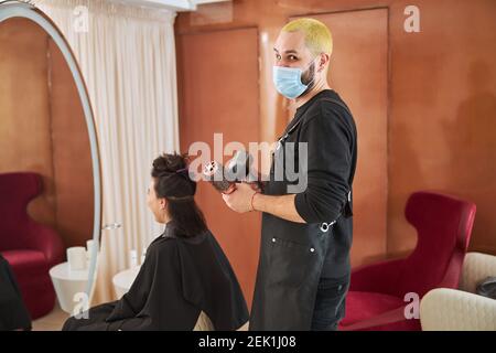 Lächelnder Stylist in einer Gesichtsmaske mit Friseurwerkzeugen Stockfoto