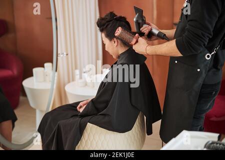 Coiffeur mit Friseurwerkzeugen hinter einer dunkelhaarigen Dame Stockfoto