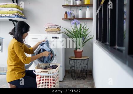 Frau vor der Waschmaschine macht Wäsche Laden von Kleidung im Inneren Stockfoto