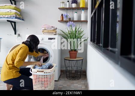 Frau vor der Waschmaschine macht Wäsche Laden von Kleidung im Inneren Stockfoto